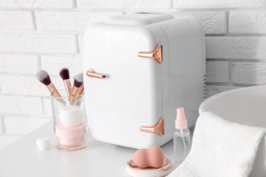 Küçük kozmetik buzdolabı, makyaj fırçaları ve sünger odadaki beyaz tuğla duvarın yanındaki masada. Yakın çekim.