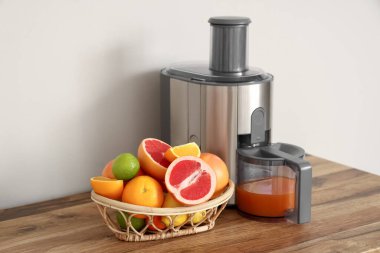 Beyaz duvarın yanındaki masada taze narenciye meyveleri olan modern meyve sıkacağı ve sepeti yakın plan.