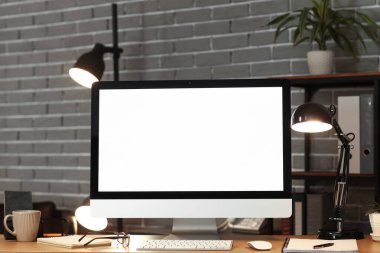 Boş bilgisayar monitörü ve parıldayan lamba karanlık ofisteki masada.