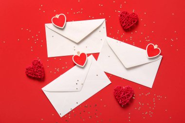 Kırmızı zemin üzerinde zarflar, kalpler ve pullar olan kompozisyon. Sevgililer Günü kutlaması