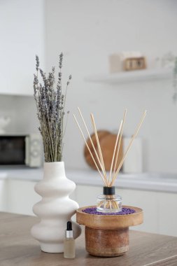 Reed yayıcı, lavanta çiçekli vazo ve mutfak masasında gerekli yağ, yakın plan.