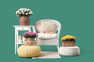 Yeşil arka planda yastıklı, dekorlu ve kasımpatı çiçekli beyaz koltuk.