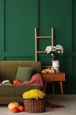 İçinde yeşil kanepe, balkabağı ve kasımpatı çiçekleri olan oturma odası.