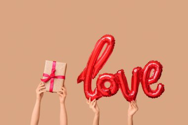 Aşk kelimesi şeklinde balonu ve bej arka planda hediye kutusu olan kadın elleri. Sevgililer Günü kutlaması