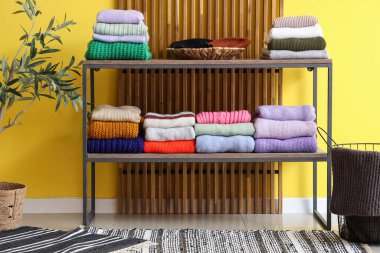 Sarı duvarın yanındaki raflarda katlanmış kışlık süveterler.