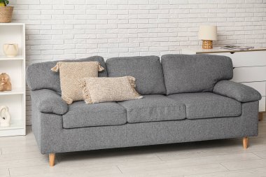 Beyaz tuğla duvarın yanında rahat kanepesi, şifoniyeri ve raf ünitesi olan şık bir oturma odası.