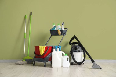 Yeşil duvarın yanında temizlik malzemeleri ve elektrikli süpürgeyle dolu bir araba.