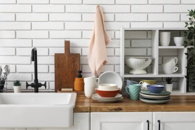 Seramik lavabo ve temiz tabaklar hafif tuğla duvarın yanındaki ahşap tezgahta.