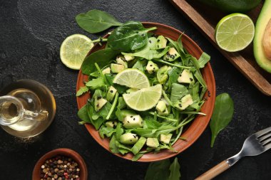 Bir kase lezzetli avokado salatası, ıspanak yaprakları ve siyah arka planda limon.
