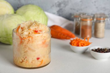 Lezzetli mayalanmış lahana kavanozu ve masadaki malzemeler gri arka planda. Yakın çekim.