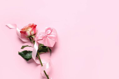 Gül çiçeği, ipek kurdele ve pembe arka planda kalp şeklinde hediye kutusu olan kompozisyon. Sevgililer Günü kutlaması.