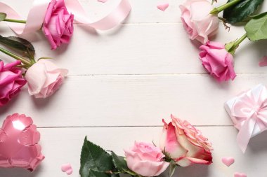 Gül çiçeklerinden yapılmış çerçeve, beyaz ahşap arka planda kağıt kalpler ve kalp şeklinde balondan yapılmış. Sevgililer Günü kutlaması