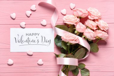 Bir buket gül çiçeği ve pembe ahşap zemin üzerinde Mutlu VALENTINE Günü yazılı tebrik kartı içeren kompozisyon. Sevgililer Günü kutlaması