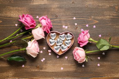 Gül çiçekli kompozisyon ve tahta arka planda kalp şeklinde şekerler olan hediye kutusu. Sevgililer Günü kutlaması