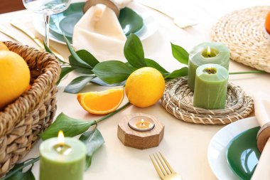 Oturma odasında turunçgiller, yanan mumlar ve yeşil yapraklarla dolu güzel bir masa.