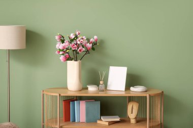 Vazoda yeşil duvarın yanında çiçek açan manolya dalları ve dekorasyonu olan raf ünitesi. Yakın çekim.