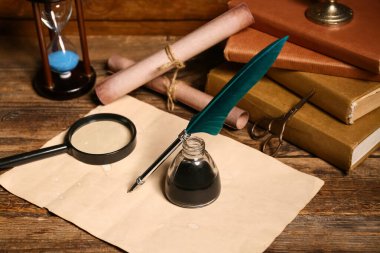 Ahşap zemin üzerinde kalem, mürekkep, parşömen, makas ve büyüteç olan eski kitaplar.