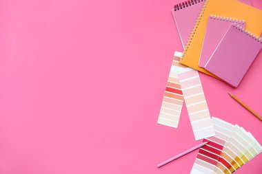 Farklı not defterleriyle kompozisyon, pembe arka planda boya paletleri ve kalemler