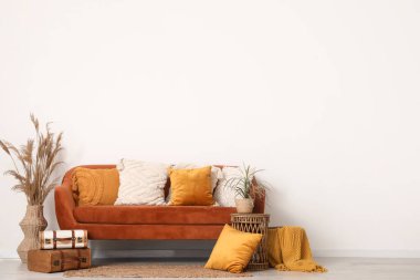 Yastıklı rahat bir kanepe, otlar ve beyaz duvarın yanındaki kahve masası.