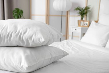 Beyaz battaniyeli rahat yatak ve şık yatak odasında yumuşak yastıklar, yakın çekim.