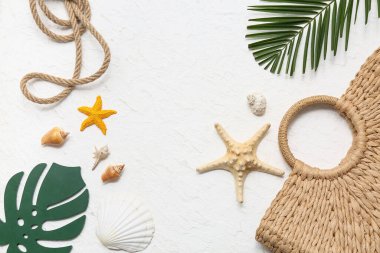 Deniz kabukları, deniz yıldızları ve beyaz arka planda palmiye yapraklarıyla dolu bir kumsal çantası.