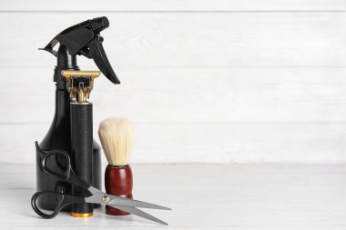 Makasla modern budama makinesi, bir şişe kozmetik ürünü ve beyaz ahşap arka planda tıraş fırçası.