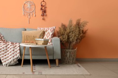 Rahat bir kanepe, masa ve vazo, mercan duvarının yanında otlar, oturma odası.