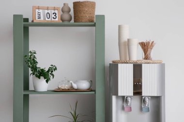 Modern su soğutucusu ve raflar beyaz duvarın yanında, yakın plan.