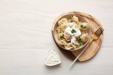 Bir kase lezzetli maydanozlu haşlanmış hamur köftesi ve beyaz ahşap arka planda ekşi krema.