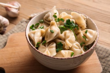 Bir kase lezzetli maydanozlu haşlanmış hamur köftesi ve ahşap arka planda sarımsak. Yakın plan.