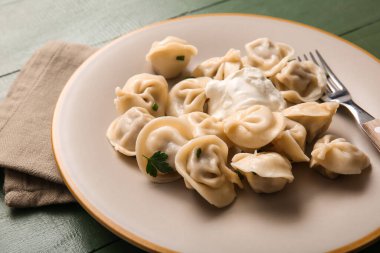 Ekşi kremalı ve yeşil ahşap arka planda maydanozlu lezzetli haşlanmış hamur köfteleri yakın plan.