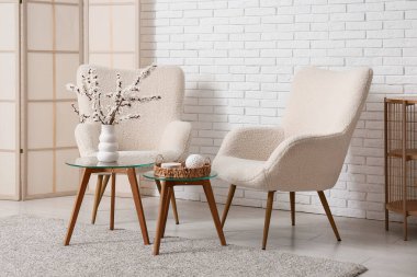 Oturma odasının içinde koltuklar, masalar ve çiçek açan dallar.