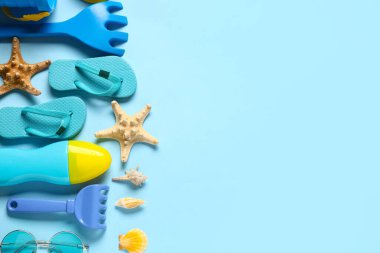 Dekoratif parmak arası terlikleri, deniz yıldızları ve mavi arka planda oyuncak tırmıkları olan kompozisyon.
