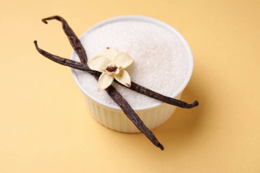 Sarı arka planda kapsüllü ve çiçekli bir kase vanilyalı şeker, yakın plan.