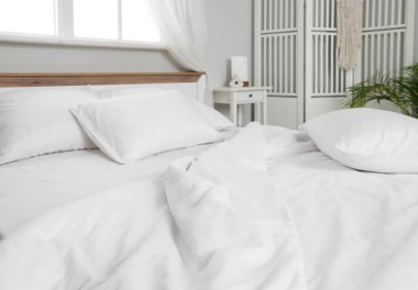 Odasında beyaz çarşaf olan rahat yatak.