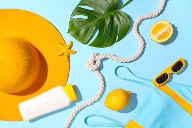 Mavi arka planda mayo, plaj aksesuarları, limonlar ve tropikal yaprak kompozisyonu