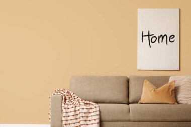 Oturma odasındaki bej duvarın yanında yumuşak yastıklı rahat kahverengi kanepe.