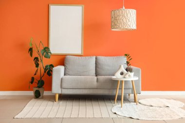 Gri kanepesi, kahve masası ve turuncu duvarın yanında bitkileri olan şık bir oturma odası.
