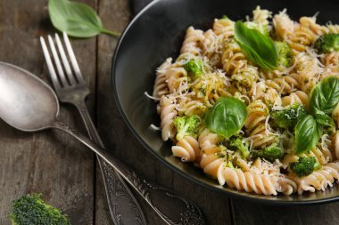 Bir kase lezzetli fusilli makarna brokoli ve ahşap arka planda fesleğen yaprakları, yakın plan.