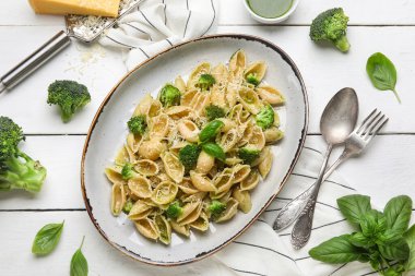 Beyaz ahşap arka planda brokoli ve fesleğen yapraklı enfes koni rigli makarna tabağı.