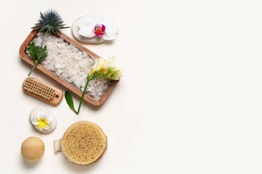 Deniz tuzu, masaj fırçası ve açık arkaplanda çiçekler içeren spa kompozisyonu