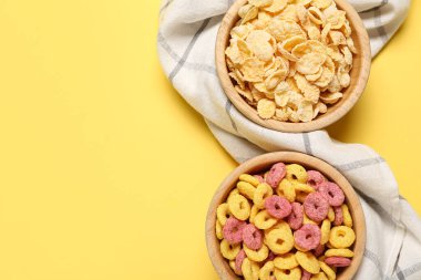 Tahta kaseler mısır gevreği ve sarı arka planda renk tahıl halkaları, yakın plan.