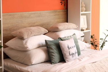 Yatak odasının iç tarafındaki turuncu duvarın yanındaki rahat yatakta farklı yastıklar var.