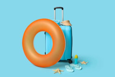 Mavi arka planda şişirilebilir yüzük, bavul ve plaj aksesuarları, yakın plan.