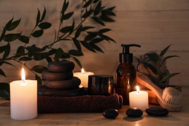 Spa taşları, yanan mumlar, kavanoz ve bir şişe kozmetik ürünü ahşap arka planda, yakın plan