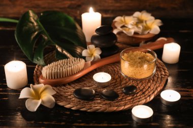 Kaplıca taşlı hasır, masaj vücut fırçası ve ahşap arka planda yanan mumlar, yakın plan.