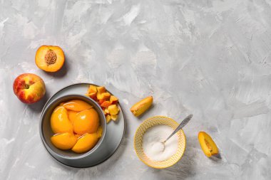 Bir kase şeftali konservesi ve açık gri arka planda şeker.