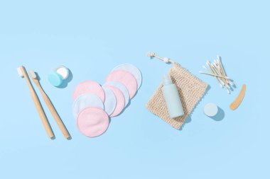 Torba, diş fırçası, bir şişe kozmetik ürünü ve mavi arka planda bezler ile yeniden kullanılabilir pamuklar.