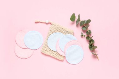 Pembe zemin üzerinde çanta ve okaliptüs dalı ile yeniden kullanılabilir pamuk pedleri