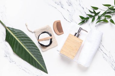 Çantalı yeniden kullanılabilir pamuk pedleri, bir şişe kozmetik, fırça, havlu ve mermer arka planda yapraklar